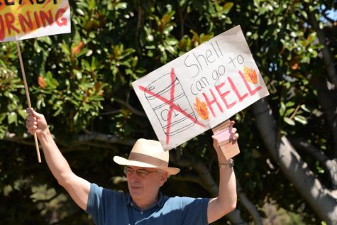 A man holds up a sign sporting “Shell can go to Hell”, protesting the harmful production and use of oil from the company.