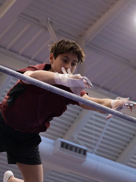 Junior Eli Wright competes in the high bar, as seen here where Wright glides in mid air trying to grasp onto the bar. 