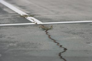 Cracks are visible on the courts near the football field, with weeds beginning to grow through them.