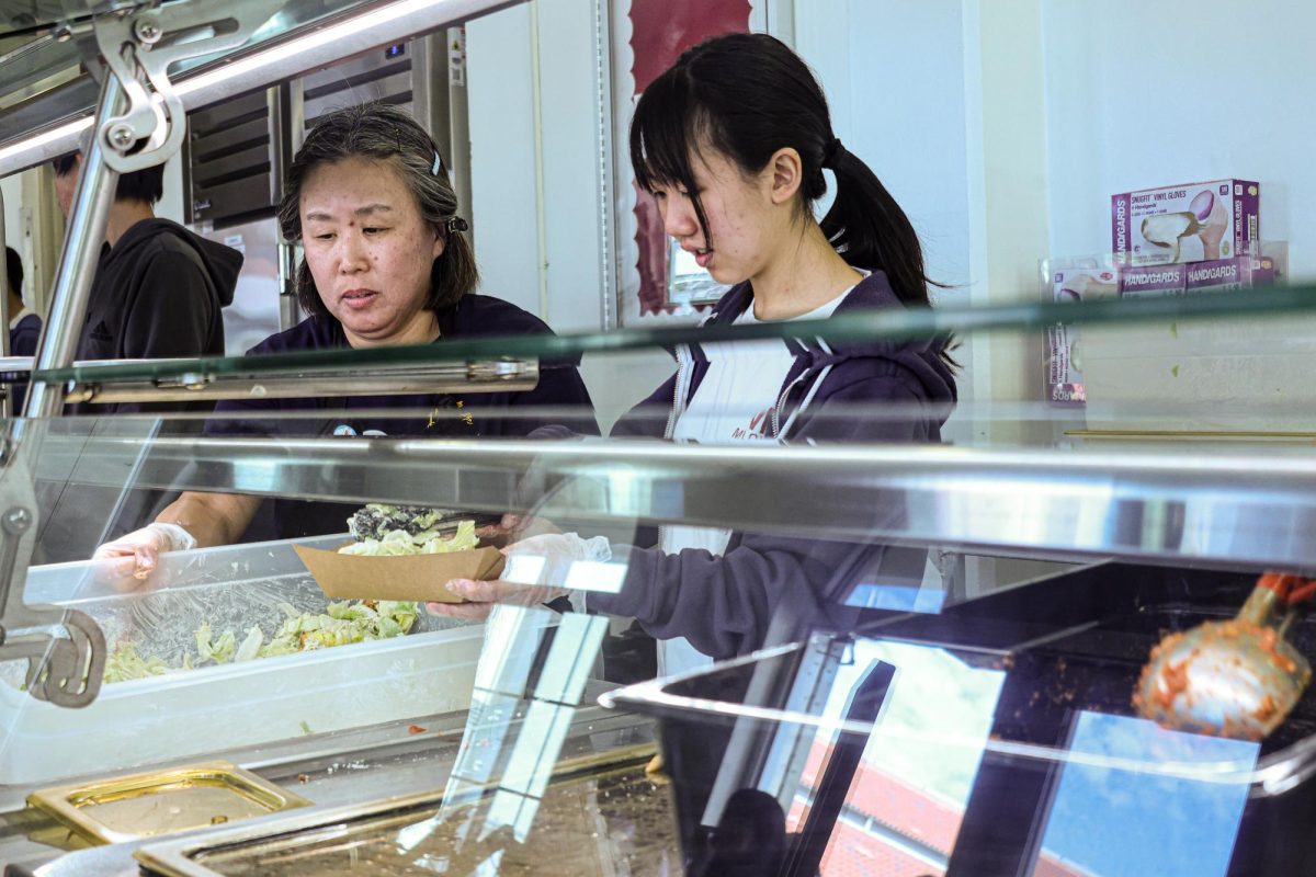 Junior Emily Zhang and cafeteria staff member Ayako Ando distribute food.
